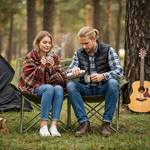 Two people sitting in chairs outdoors, surrounded by trees, with a guitar leaning against a tree.