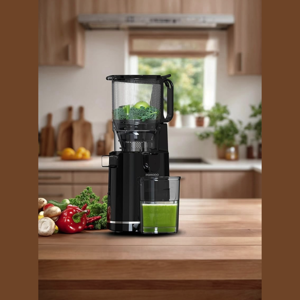 Black juice extractor on a kitchen counter with green juice and vegetables, surrounded by a kitchen setting.