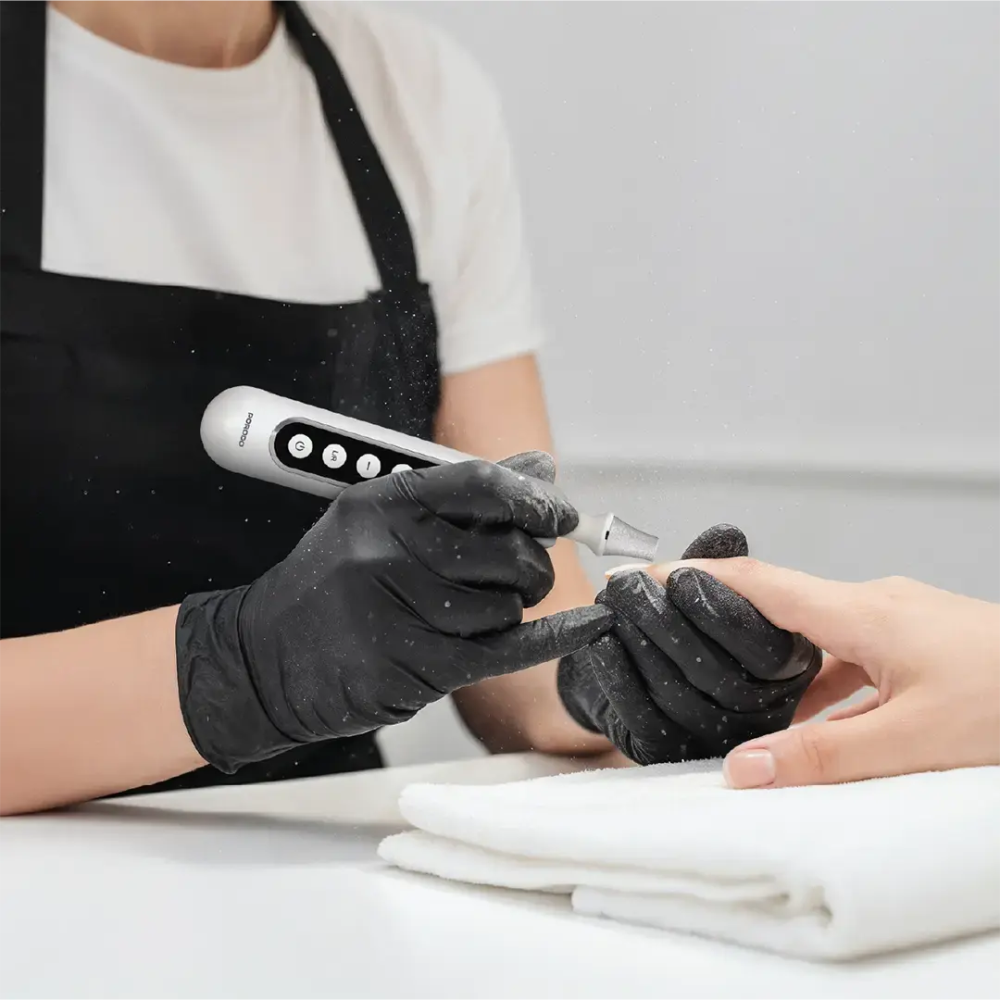 Person getting a manicure with black gloves and a white light device.